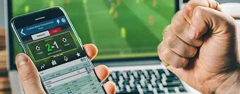 person holding a phone with a sports betting app and laptop